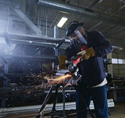 Photo of worker using CRAFTSMAN angle grinder CMCG450B, producing sparks while cutting metal pipes in an industrial workshop.
