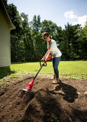 Photo of CRAFTSMAN cordless cultivator CMCTL320B in use in a garden, person tilling soil outdoors.